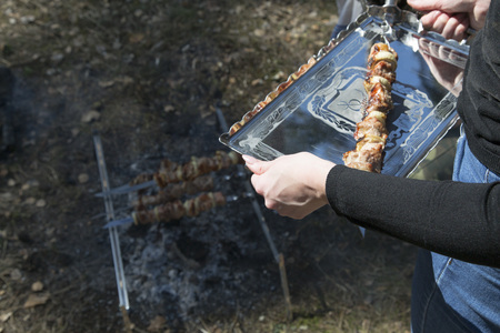 A woman is holding a tray with a shish kebab. Outdoor bbq party concept. Early spring day. Meat background. Side view.の写真素材