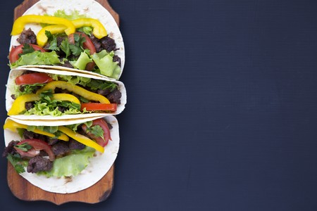 Tacos with meat and vegetables on the board on a black wooden background, top view. Black background...