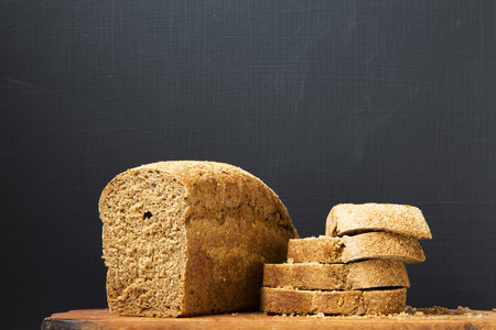 Sliced bread on wooden board. Dark background. Side view. Copy space.