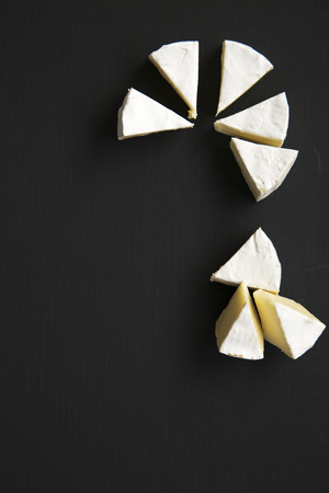 Slices of cheese camembert or brie on dark background. Milk production. Top view. Flat lay. Copy...