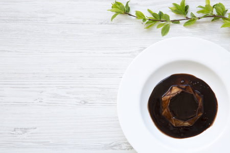 Panacotta dessert with chocolate in white plate on white wooden background decorated with blossoming cherry branch. Flat lay. Top view. From above. Copy space.の写真素材