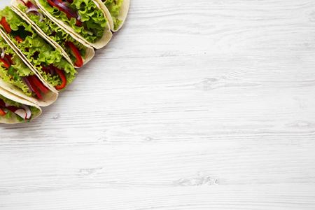Corn tortillas with lettuce, redish, cucumber, onion, parsley and pepper on white wooden table, from above. Top view. Copy space.の写真素材