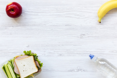 Healthy school lunch box with sandwich, fruits and bottle of water on white wooden background, flat lay. From above. Copy space.の写真素材