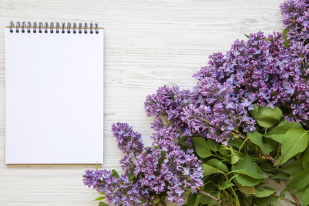 A bouquet of lilac flowers with notebook on a white wooden background. Mothers Day. Copy space. From above, flat lay.の写真素材