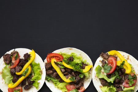 Mexican tacos with beef and vegetables, beer and lime on a black background, top view. Copy space....