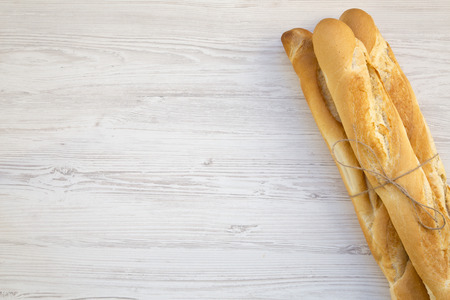 Fresh french baguettes on white wooden background, top view. Copy space.