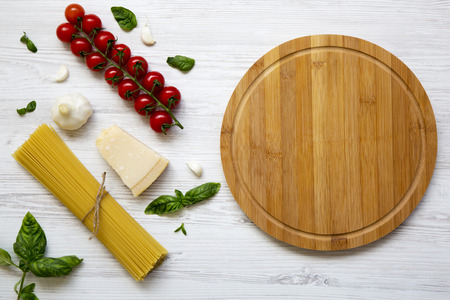 Round wooden board with spaghetti, tomatoes, basil, parmesan, garlic. Ingredients for cooking...