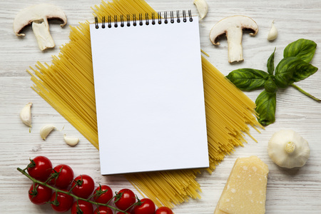 Different ingredients for cooking pasta with notebook on a white wooden background. Top view. Flat...