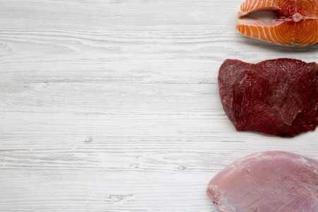 Uncooked raw salmon steak, beef meat and turkey breast on white wooden background, top view. Flat lay. Copy space.の写真素材