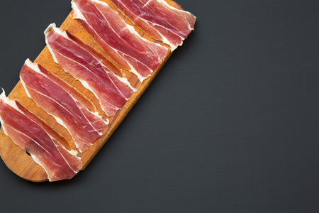 Sliced jamon Serrano or Iberico on cutting wooden board. Traditional spanish hamon on dark wooden background, top view. Copy space.の写真素材