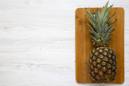 A large ripe pineapple on a bamboo cutting board. White wooden background, top view. From above. Copy space.の写真素材
