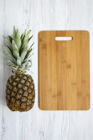 Large ripe pineapple with bamboo cutting board. White wooden background, top view. From above.  Flat lay. Copy space.の写真素材