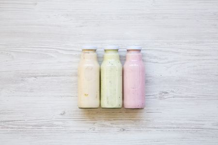 Fruit smoothies of different colors in glass jars on white wooden background. Top view, from above. の写真素材