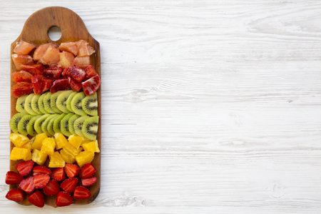 Chopped fresh fruits arranged on cutting board on white wooden background with copy space, top view. Ingredients for fruit salad. From above, flat lay, overhead.の写真素材