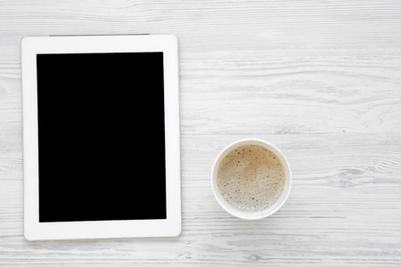 Minimal work space with tablet and latte on white wooden background, top view. Flat lay. Copy space.