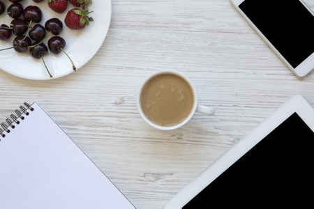 Work space with smartphone, strawberries, cherries, notepad and latte in the center on white wooden background. Top view.の写真素材
