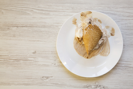 Ice cream cone on a white plate. Melting scoops. White wooden background. Top view. From above, flat...