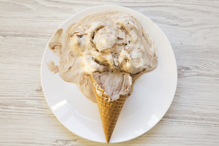 Ice cream cone on a white plate. Melting scoops. White wooden background. Top view. From above, flat...