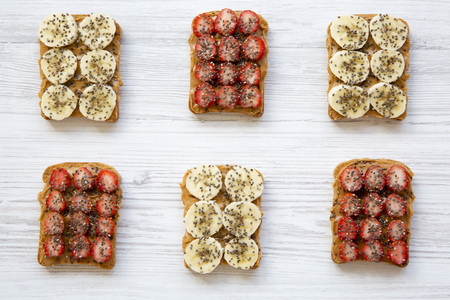 Healthy breakfast. Vegan toasts with peanut butter, fruits and chia seeds on white wooden background, top view.の写真素材
