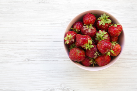 Fresh strawberries in a pink ceramic bowl on white wooden background, top view. From above. Copy space.の写真素材
