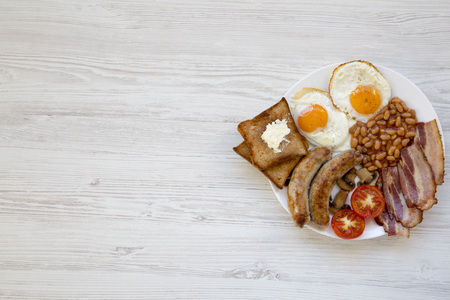English breakfast with fried eggs, sausages, beans, bacon and toasts over white wooden background. Top view. Flat lay. From above, overhead. Copy space.の写真素材