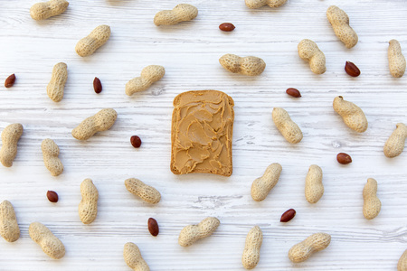 Single toast with peanut butter and peanuts on a white wooden background, top view.の写真素材