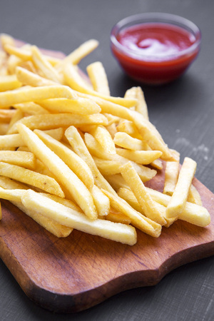 Side view french fries with ketchup over black background. Close-up.