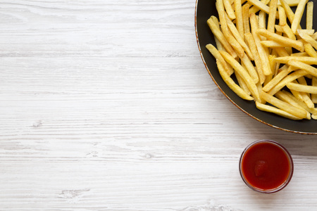 French fries in a frying pan with ketchup on a white wooden table, top view. Copy space.