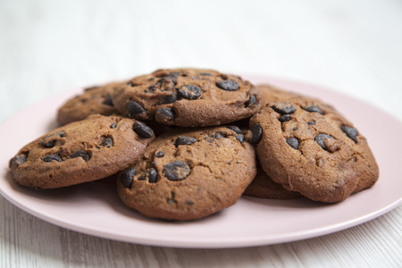 Tasty chocolate cookies on a pink plate on a white wooden table, side view. Closeup.