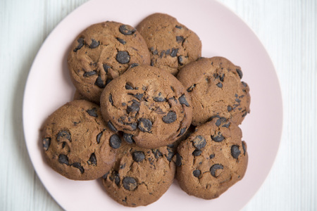 Delicious chocolate cookies on a pink plate on a white wooden table, top view. From above. Closeup.