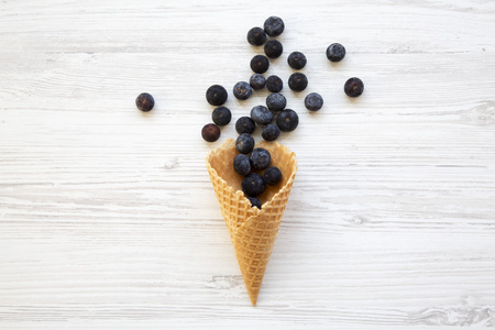Flat-lay of waffle sweet ice cream cone with blueberries on a white wooden background.の写真素材