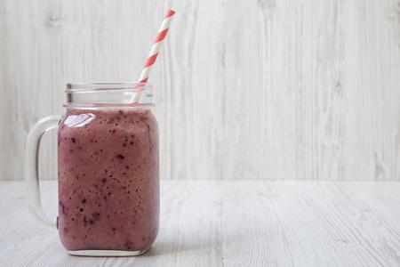 Glass jar with berry smoothie made of banana, black currant, coconut milk on a white wooden background, side view. Copy space.の写真素材