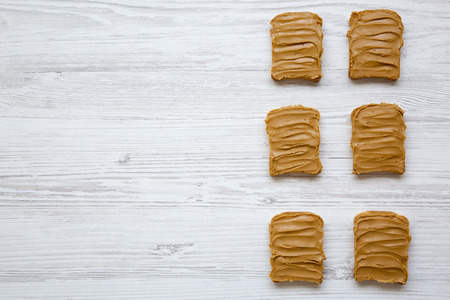 Peanut butter toasts on a white wooden background, from above. Top view. Copy space.