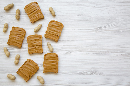 Peanut butter toasts and unshelled peanuts on a white wooden background, top view. Copy space. From above.の写真素材