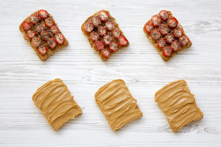 Top view, toasts with peanut butter, strawberries and chia seeds on white wooden surface. Healthy...
