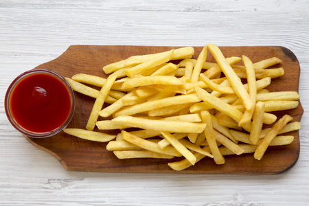 French fries with sauce on wooden board over white wooden surface, top view. From above.