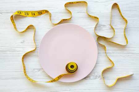 Pink plate with measuring tape on  white wooden background, top view. From above, flat lay. Dieting concept.の写真素材