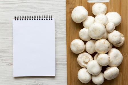 Champignon mushrooms on bamboo board with notepad over white wooden background, top view. From above.の写真素材