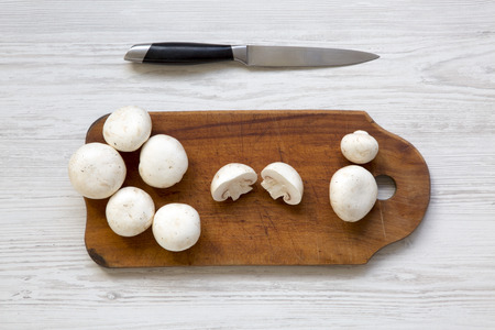 Champignon mushrooms on wooden board with knife over white wooden background, top view. From above.の写真素材