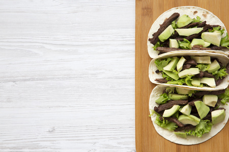 Tortillas with grilled beef and avocado on the bamboo board on a white wooden table. Top view, from above. Copy space.の写真素材