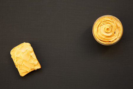 Bowl of peanut butter and toast on a black background, top view. From above.