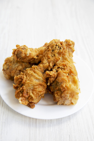 Fried chicken legs on a white plate over white wooden surface, close-up. Side view.の写真素材