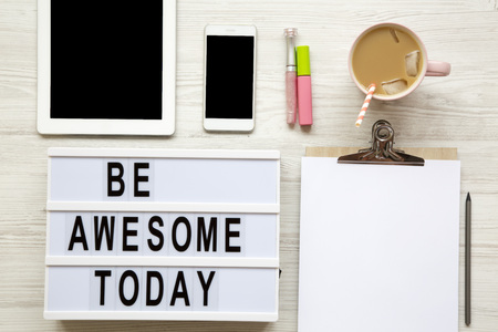Feminine workplace with tablet, noticepad, sheet, latte ice and 'Be awesome today' words on modern board over white wooden surface, top view.の写真素材