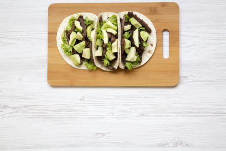From above, tortillas with grilled beef and avocado on the bamboo board over white wooden surface. From above, overhead. Copy space.の写真素材