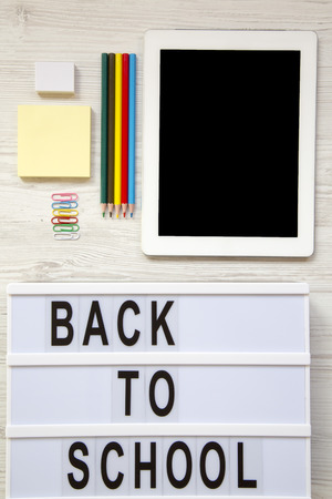Tablet, eraser, pencils, stickers, paper clips and 'Back to school' word on a modern board over a white wooden desk. Top view, from above.の写真素材
