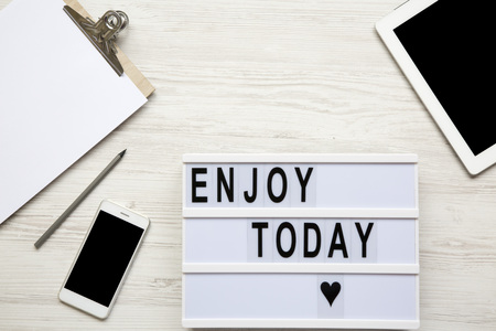 Work space with tablet, smartphone, notepad and 'Enjoy today' word on lightbox over white wooden background, top view. From above, flat-lay, overhead. Copy space.の写真素材