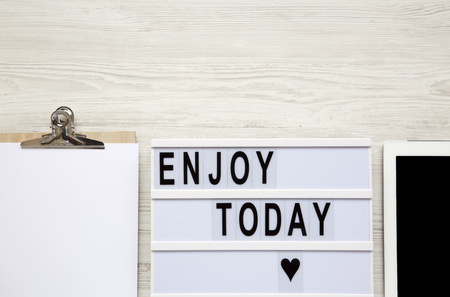Work space with tablet, notepad and 'Enjoy today' word on lightbox over white wooden surface, top view. From above, flat-lay, overhead. Copy space.の写真素材