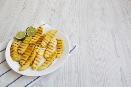 Grilled pineapple slices with lime on white plate over white wooden background, side view. Summer food. Idea for snack. Copy space and text area.の写真素材