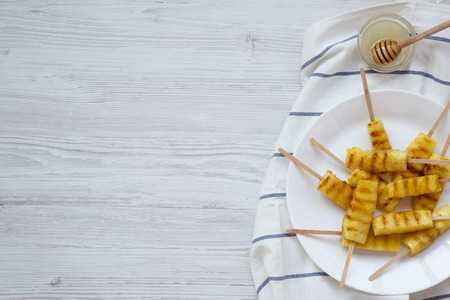 Grilled pineapple on bamboo sticks with honey on a white wooden table, view from above. Top view, flat lay, overhead. Space for text.の写真素材