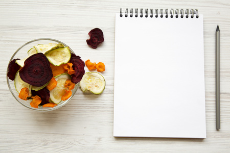 Full bowl of veggie chips with notepad on white wooden table, top view. From above, overhead. Close-up.の写真素材